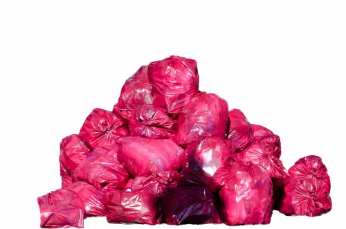 A collection of multiple pink plastic rubbish bags piled together on a white background, with some bags appearing to be loosely tied and others more firmly sealed. The bags vary slightly in size and shape, with some showing creases and wrinkles on their surfaces. The pile is set in an open, well-lit environment, likely on a flat surface such as a pavement or driveway, and is situated centrally in the image. The overall scene suggests waste ready for collection, relevant to the rubbish removal services offered by Commercial Waste Removal Eltham in the local area, such as Eltham or nearby London suburbs.